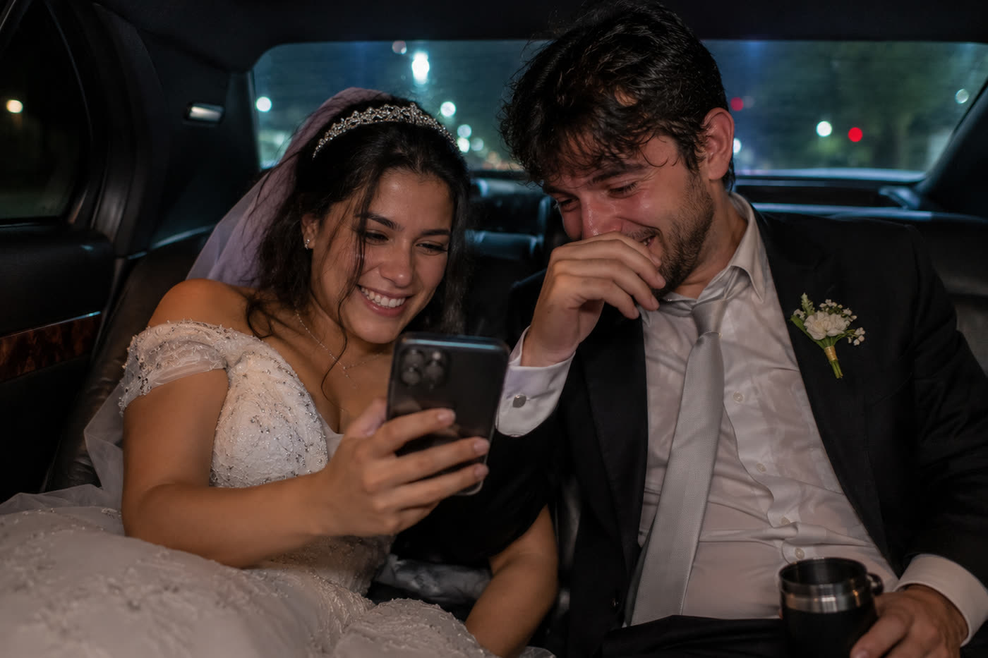 Noivos sentados no carro à noite, rindo juntos do que ouvem no celular