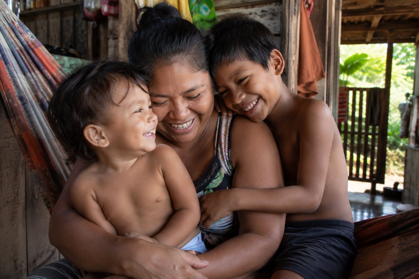 Mãe sorridente com o filho bebê no colo, num jardim florido