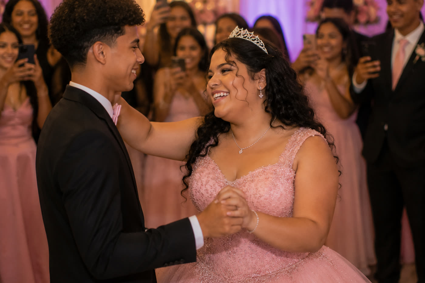 Debutante de vestido rosa dançando a valsa enquanto os convidados filmam pelo celular